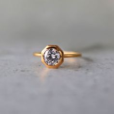 a gold ring with a white diamond in the center on a gray surface, close up