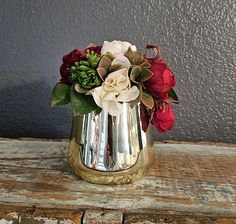 a gold vase with red and white flowers in it on a wooden table next to a gray wall