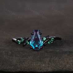 an unusual ring with blue and green stones on it's sides, sitting on top of a rock