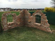 an old brick wall with arched windows and bars on the top, surrounded by green grass