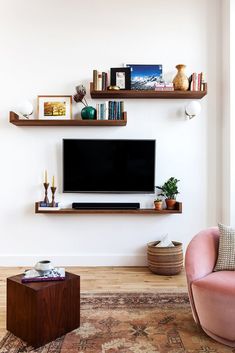 a living room with two shelves and a tv on the wall above it is a pink chair