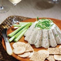 a plate with crackers, celery and cheese on it next to a glass of wine