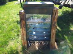 a metal box sitting in the grass next to a wooden pole and some pipes on top of it