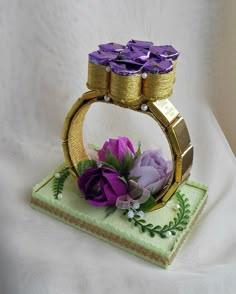 a gold ring with purple flowers in it sitting on a green napkin and white cloth