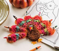 a crocheted turkey sitting on top of a table next to two pumpkins