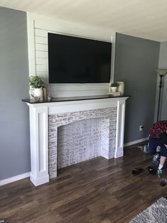 a boy sitting on the floor in front of a fireplace with a tv above it