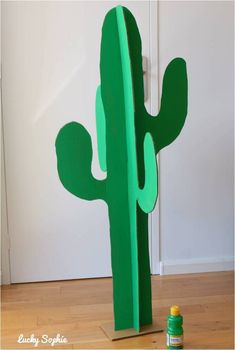 a cardboard cactus sitting on top of a wooden floor next to a green spray bottle