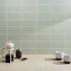 two mugs and one teapot sit on a counter in front of a tiled wall