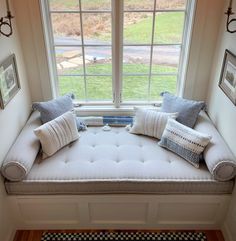 a window seat in the corner of a room with pillows and pictures on the wall