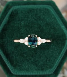 an emerald colored ring with three diamonds on it in a green velvet box, sitting on top of a carpeted surface