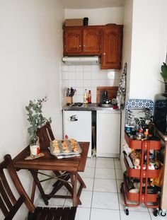 a small kitchen with white tile flooring and wooden cabinets, along with a table that has food on it