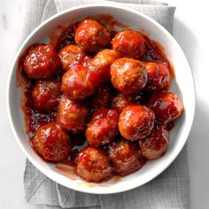 a white bowl filled with meatballs covered in ketchup on top of a gray napkin