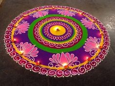 a colorful rangdi design on the ground with lit candles and flowers in the center