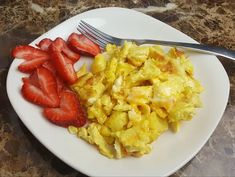 scrambled eggs and strawberries on a white plate with a fork next to it, sitting on a marble counter top