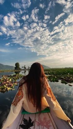 a woman riding on the back of a boat down a river filled with lily pads