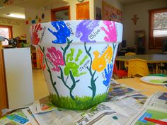 a flower pot painted with handprints sitting on top of a pile of newspapers