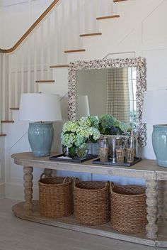 a table with baskets and vases on it in front of a stair case next to a mirror