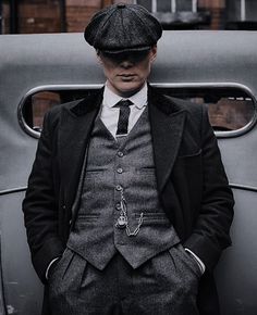 a man in a suit and hat standing next to an old car