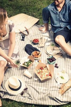 a man and woman sitting on a blanket at a picnic with plates of food in front of them