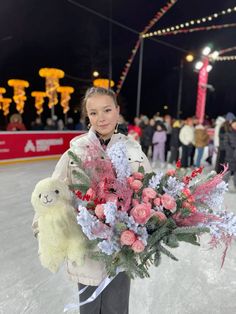 a woman holding a bouquet of flowers and a teddy bear in front of an ice rink