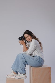 a woman sitting on top of a wooden block with a camera in front of her