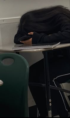 a woman sitting at a desk with her head in her hands while holding a cell phone