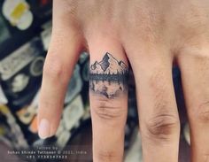 a person's hand with a small mountain tattoo on the middle finger and an arrow in the middle