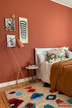 a bedroom with an orange wall and white bed in the corner, two pictures on the wall