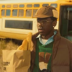 a man in glasses and a hat holding a paper bag with food on it next to a school bus