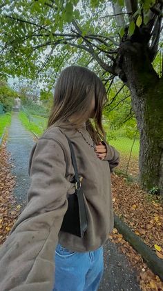 a woman is walking down the road with her hand on her hip and looking at trees