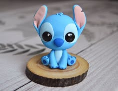 a small blue figurine sitting on top of a piece of wood with eyes wide open