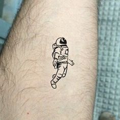 a man's arm with a small black and white astronaut tattoo on the wrist