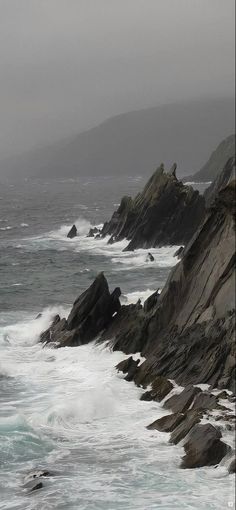 the ocean is choppy with waves coming in and crashing against the rocky shoreline on an overcast day