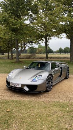 a silver sports car parked in the middle of a dirt road next to some trees