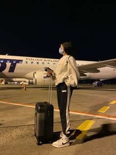 a woman standing on the tarmac with her luggage and wearing a facemask