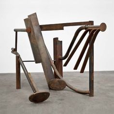 an abstract sculpture made out of wood and metal tubes on concrete flooring with white wall in background