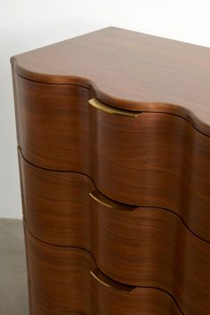 a large wooden dresser with three drawers and gold pulls on the bottom drawer, against a white wall