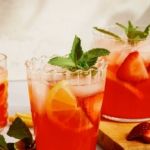 three glasses filled with strawberry lemonade and mint garnish on top of a cutting board