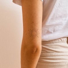 a person with a sun tattoo on their arm, standing in front of a white wall