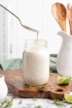 a spoon is being used to dip into a jar filled with white sauce on a cutting board