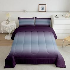 a bed with purple sheets and pillows in a room next to a white table,