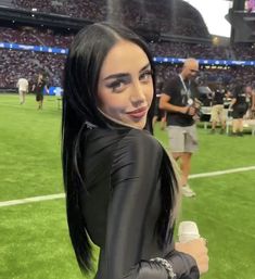 a woman with long black hair holding a microphone in front of a crowd at a football game