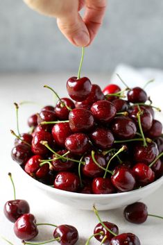 a person picking cherries from a white bowl