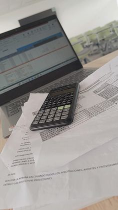 a calculator sitting on top of papers next to a laptop computer