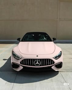 the front end of a pink car parked in a parking lot next to a building