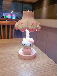 a hello kitty lamp sitting on top of a wooden table next to a cupcake