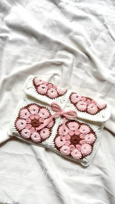 a pink and white crocheted purse on top of a white sheet with flowers