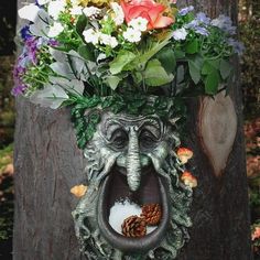 an elephant head with flowers in it's mouth on top of a tree trunk