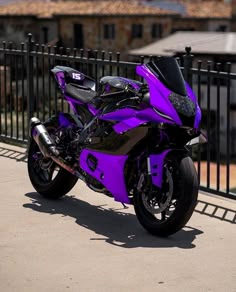 a purple motorcycle parked on the side of a road next to a black metal fence