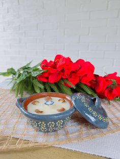 a bowl of pudding sitting on top of a table next to red flowers and greenery